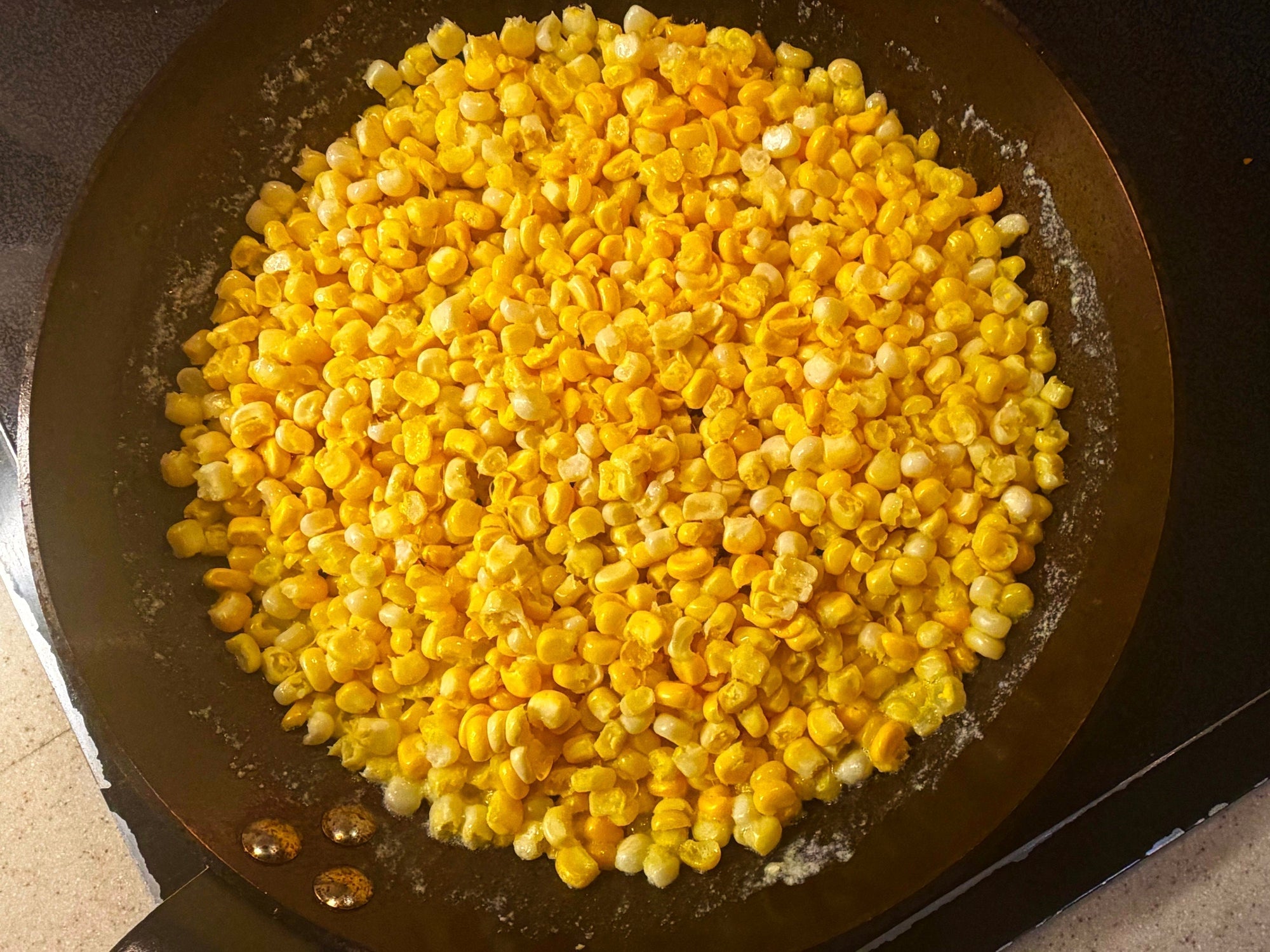 corn kernels being fried in a carbon steel pan